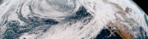 A satellite captures an atmospheric river from space. The white, banding plumes stretch across the Pacific and make landfall on the U.S. West Coast, with the curvature of Earth still in frame.
